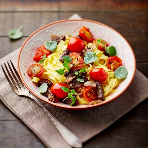 Eine Schüssel Pasta mit Tomaten, Kräutern und Oliven liegt auf einem rustikalen Holztisch. Daneben befindet sich eine Stoffserviette mit einer Gabel, während frische Oreganoblätter die Speise garnieren.