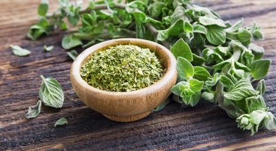 Holzschale mit getrocknetem Oregano auf einem Holztisch, daneben frische Oregano-Zweige mit grünen Blättern, die lebendig und aromatisch wirken.