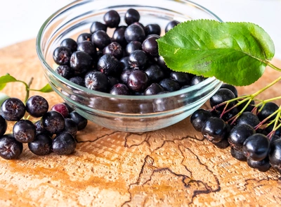 Reife Aronia-Beeren in einer Glasschale mit grünem Blatt.