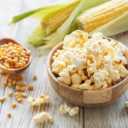 Popcorn in einer Schale mit Maiskörnern und Kolben im Hintergrund.
