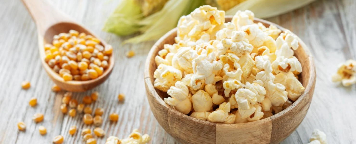 Popcorn in einer Schale mit Maiskörnern und Kolben im Hintergrund.