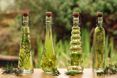 Vier Glasflaschen mit aromatisiertem Öl oder Essig, jeweils mit frischen Kräutern wie echtem Thymian gefüllt, auf einer Holzoberfläche mit unscharfem grünen Hintergrund.