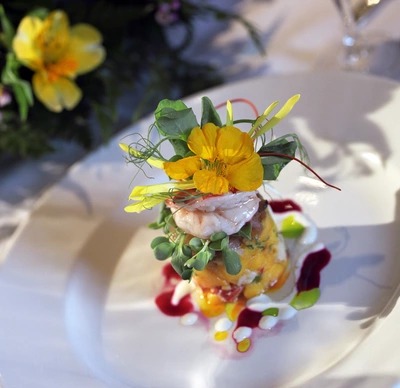 Ein elegant angerichtetes Gourmetgericht, dekoriert mit essbaren gelben Blüten der Kapuzinerkresse und frischen Kräutern. Die bunte Präsentation kombiniert kulinarischen Genuss mit ästhetischem Flair auf einem weißen Teller.