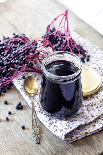 Glas mit dunklem Holunderbeerensaft oder -sirup aus Sambucus nigra mit frischen Beeren.