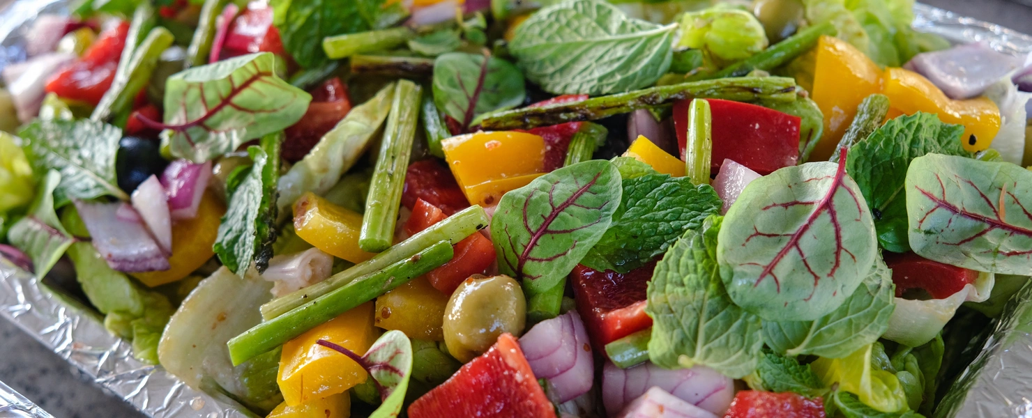 Ein bunter Salat mit frischen Zutaten wie Paprika, Zwiebeln, grünem Gemüse und Blut-Sauerampfer (Rumex sanguineus) Blättern. Die leuchtend roten Adern der Blätter ergänzen die Farben der anderen Zutaten und verleihen dem Gericht eine ansprechende Optik.