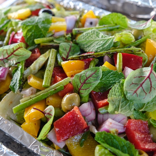 Ein bunter Salat mit frischen Zutaten wie Paprika, Zwiebeln, grünem Gemüse und Blut-Sauerampfer (Rumex sanguineus) Blättern. Die leuchtend roten Adern der Blätter ergänzen die Farben der anderen Zutaten und verleihen dem Gericht eine ansprechende Optik.