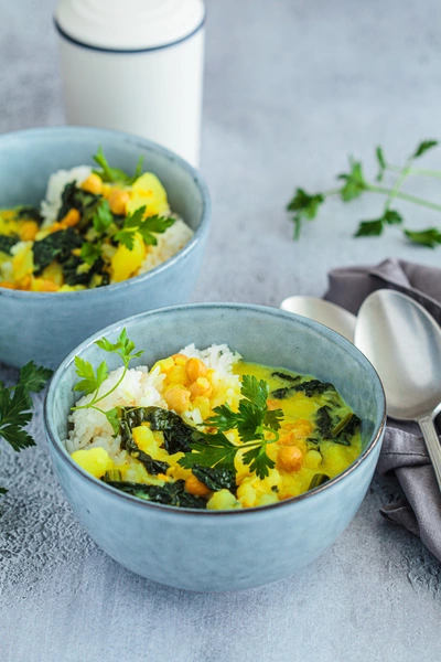 Zwei Schalen mit einer Suppe oder einem Eintopf, garniert mit frischer Glatter Petersilie (Petroselinum crispum). Die Suppe enthält verschiedene Zutaten wie Gemüse und ist auf einem stilvollen Tisch angerichtet.