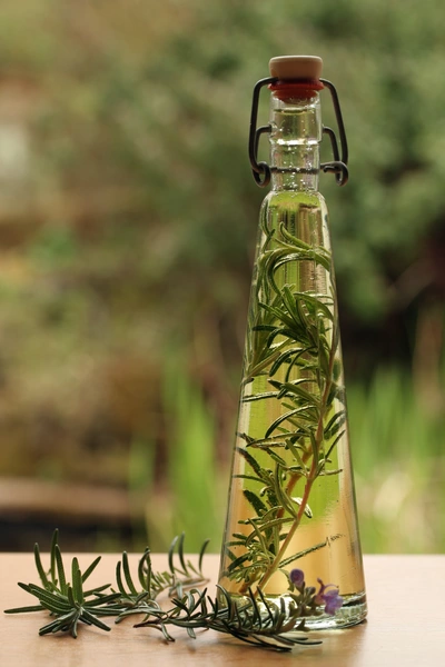 Ein Glasfläschchen mit Gourmet-Rosmarin (Salvia rosmarinus) ist mit aromatischem Öl gefüllt. Die Rosmarinzweige stehen im Öl und verleihen dem Getränk oder der Zubereitung einen intensiven Kräutergeschmack.