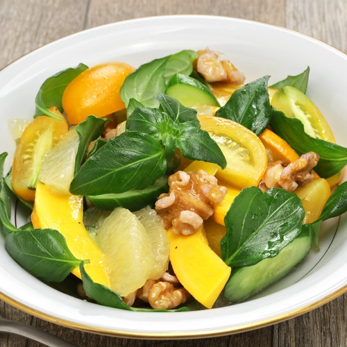 Pilzkraut (Plectranthus amboinicus) in einem frischen Salat mit Mango, Walnüssen und verschiedenen Gemüsesorten, der in einer weißen Schale angerichtet ist.