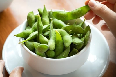 Schüssel mit grünen Edamame-Schoten, von einer Hand aufgenommen.