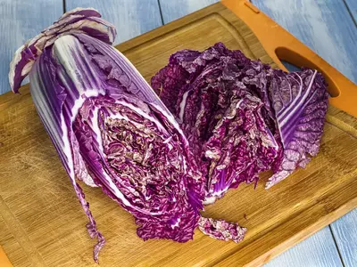Aufgeschnittener roter Chinakohl auf Holzbrett mit deutlicher Struktur der violetten Blätter.