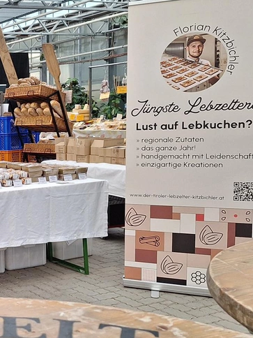 Man sieht ein Roll-Up neben einem Marktstand mit frischem Brot, Lebkuchen und anderen Lebensmitteln.