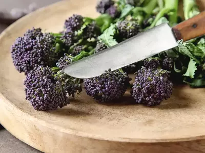 Wilder Brokkoli mit violetten Köpfen und Messer auf Schneidebrett.